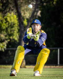 Cricket wicketkeeper with intense focus catching the ball during a match.