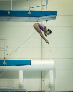 Laura Hingston mid-dive from the 10m platform with arms stretched wide and legs straight, captured in midair.