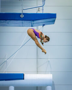 Laura Hingston mid-dive from the 10m platform with arms stretched wide and legs straight, captured in midair.