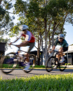 Two cyclists race past at speed with motion blur, photographed from a low angle beside the road during a criterium race.