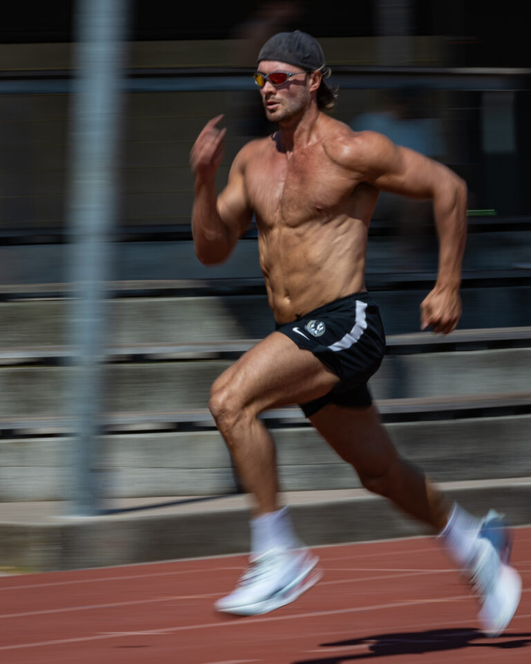 An athlete sprints down a running track at full speed, captured with motion blur to emphasise movement and intensity.