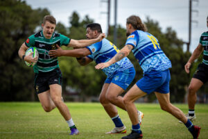 A rugby player fights through two defenders while carrying the ball during a Victorian rugby union match.