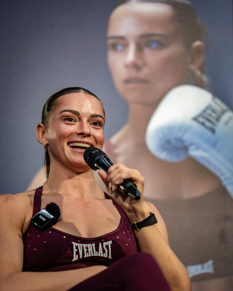 Australian boxer Skye Nicolson speaks into a microphone during an Everlast event, seated in front of a large promotional portrait backdrop.